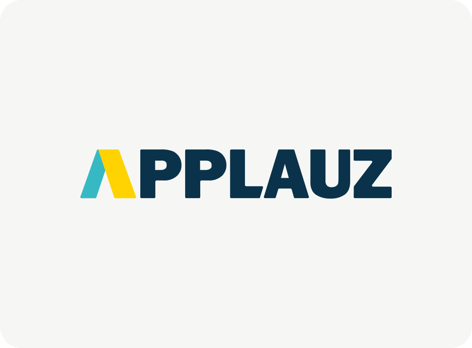 L'image affiche le mot « APPLAUZ » en lettres majuscules bleu foncé et en gras. La première lettre « A » est stylisée avec une séparation de couleurs bleu sarcelle et jaune. Le fond est gris clair.