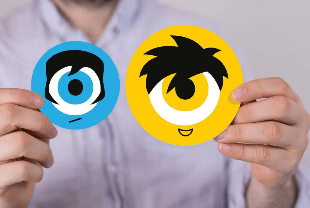 A person in a light-colored shirt holds two round cartoon face stickers: one blue with a sad expression, the other yellow with a happy expression. Both feature large single eyes and stylized hair.