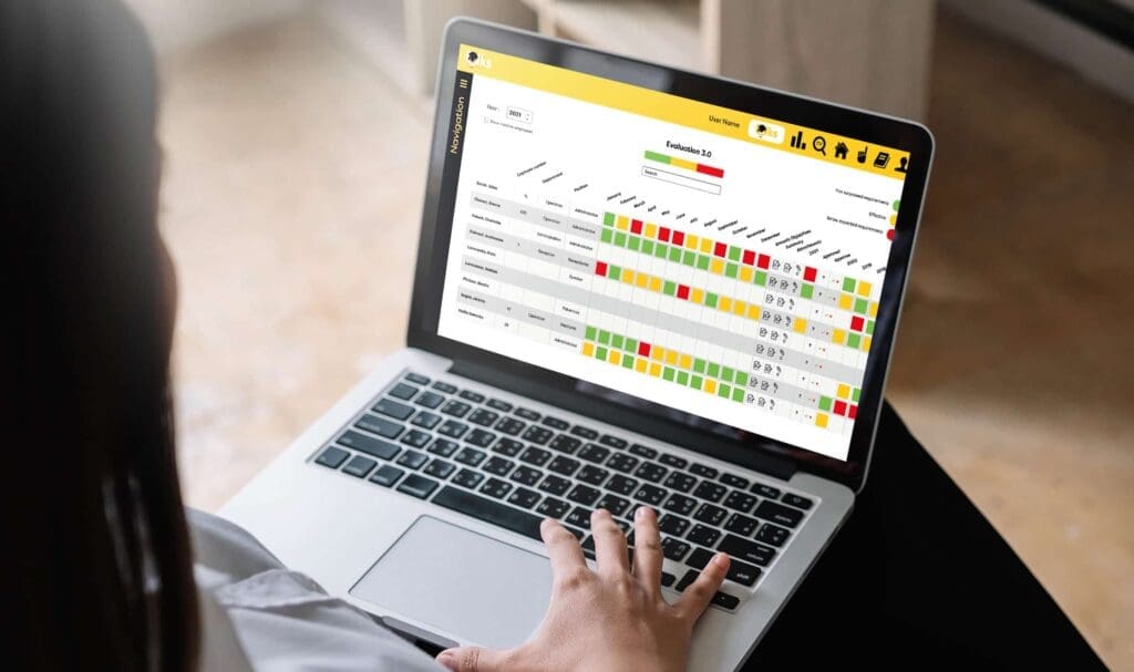 Une personne utilise un ordinateur portable affichant un tableau de bord de données coloré avec des lignes, des colonnes et des cases de différentes couleurs, représentant probablement un système d’évaluation des performances ou de suivi des progrès.