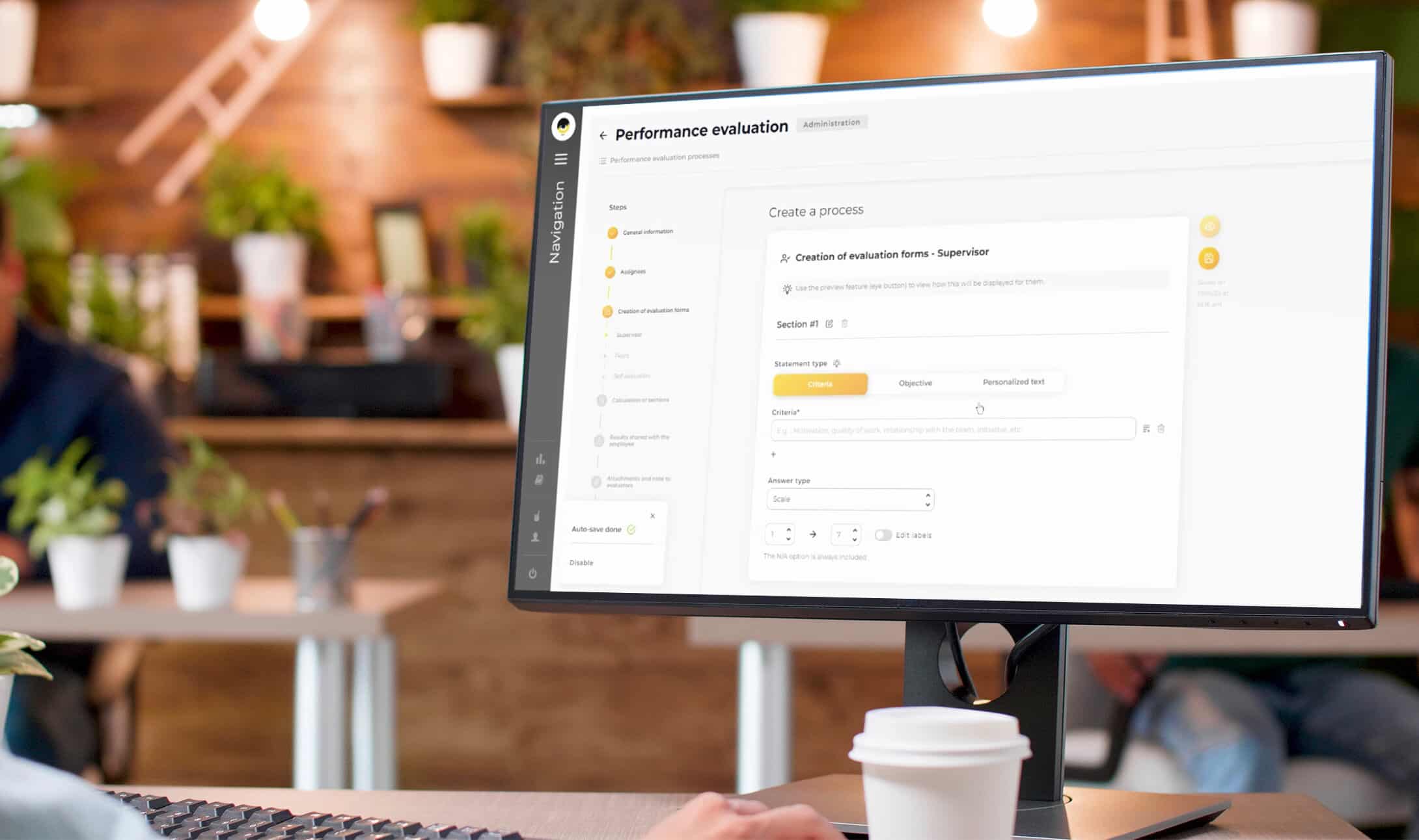 Une personne travaille à un bureau avec une tasse de café, regardant un écran d'ordinateur affichant une interface de formulaire d'évaluation des performances dans un bureau avec des collègues flous et des plantes en arrière-plan.
